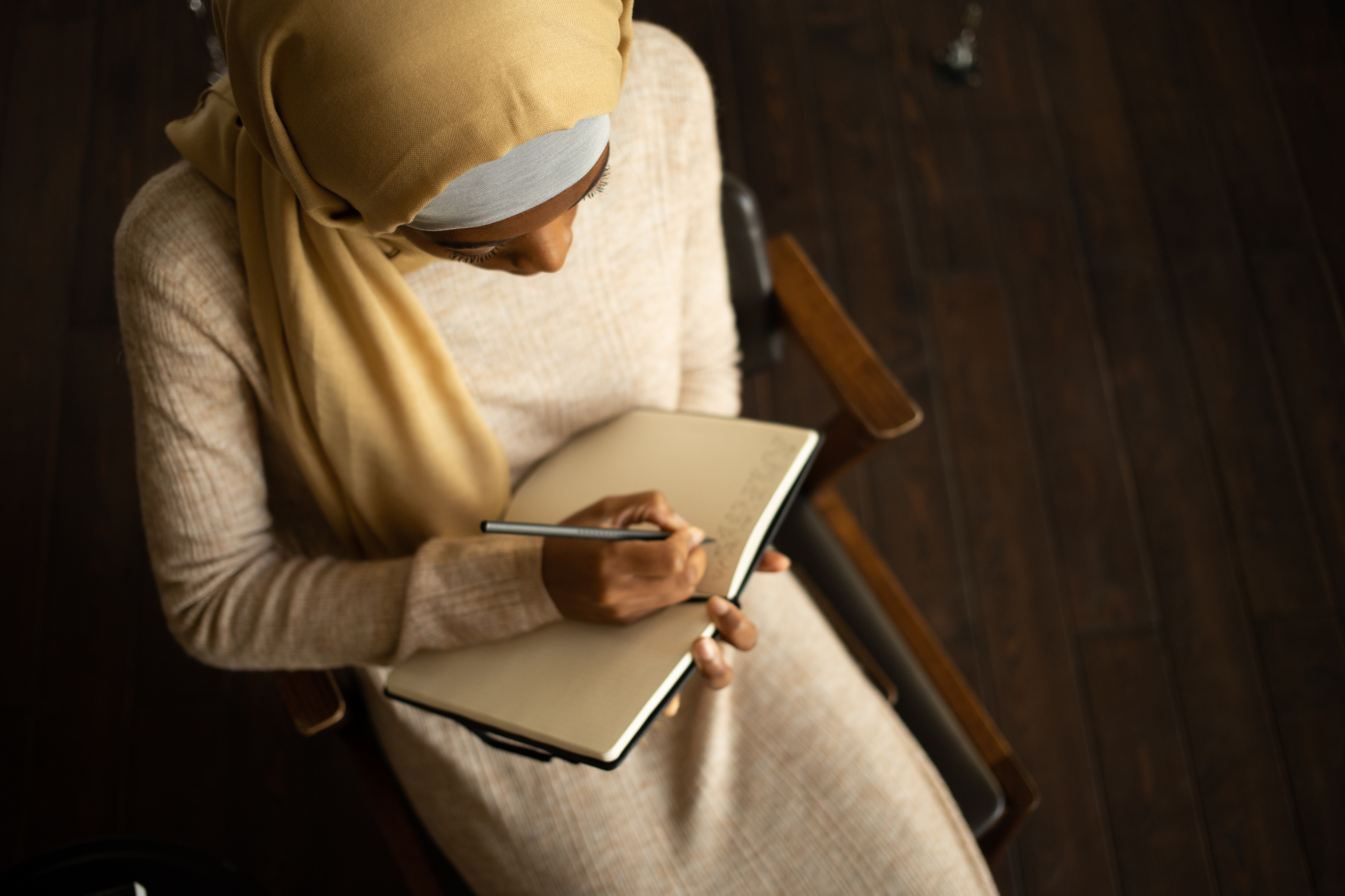 Crop black Muslim woman writing in planner